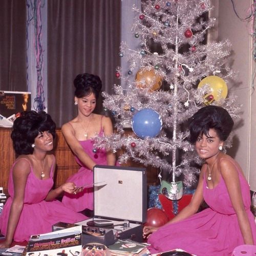 The Supremes, 1964. Three beautiful ladies wearing magenta dresses sit in front of a white aluminum Christmas tree, posing with a record player.